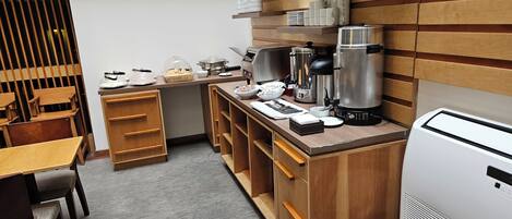 Una kitchenette compacta con muebles de madera, una cafetera y un refrigerador pequeño.
