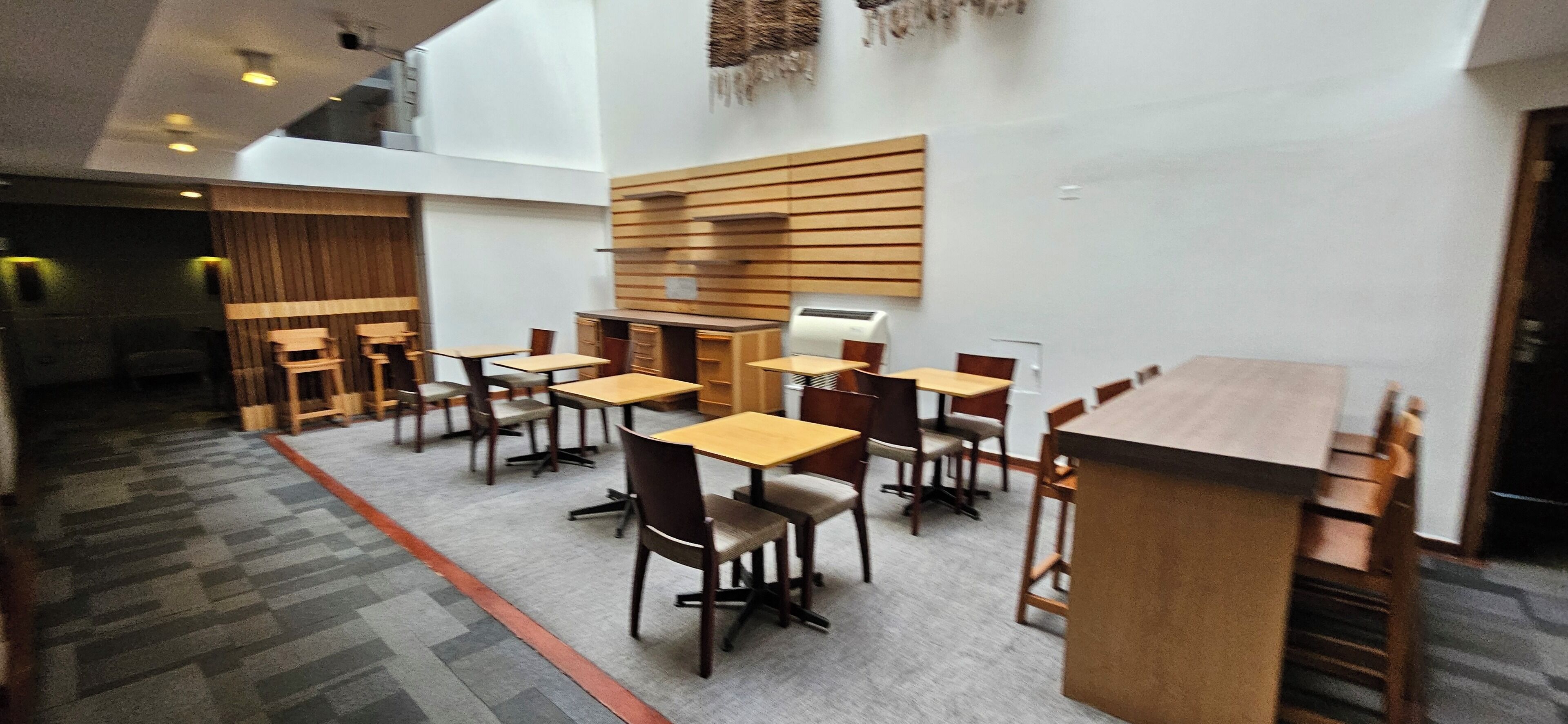 Un espace de restauration moderne avec des tables et des chaises en bois, un plafond haut et un tapis à motifs.