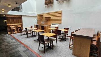 Un espace de restauration moderne avec des tables et des chaises en bois, un plafond haut et un tapis à motifs.