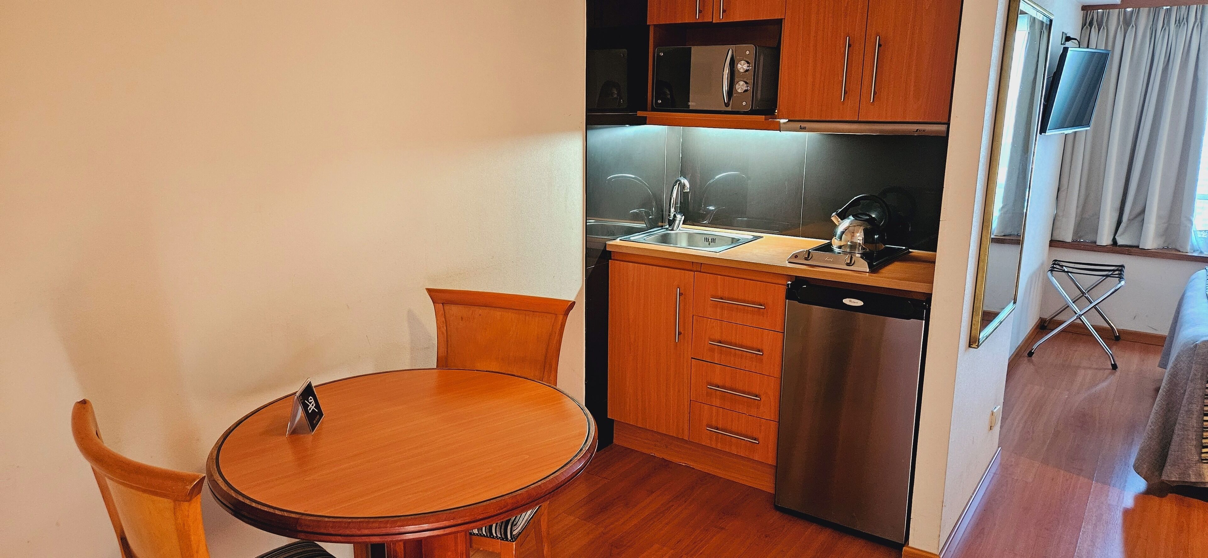 Una cocina compacta con armarios de madera, lavavajillas de acero inoxidable, microondas y un fregadero.