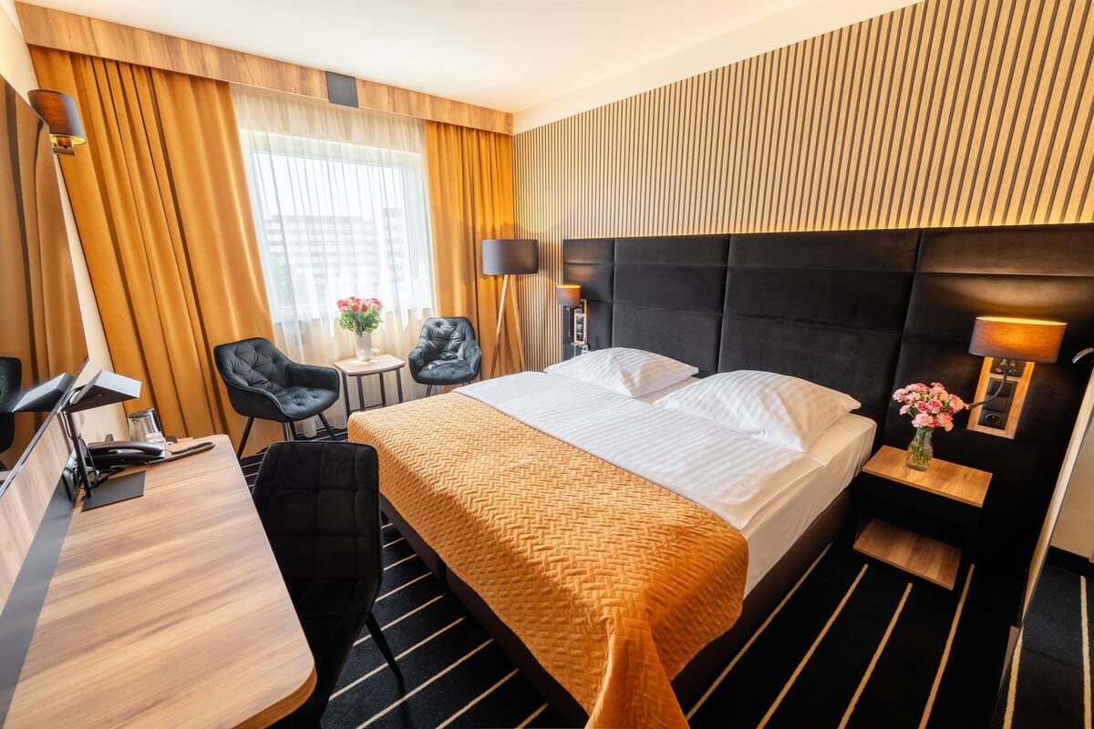 Een hotelkamer met een bed, een bureau, twee stoelen, een kleine tafel met een bloevas en een lamp.