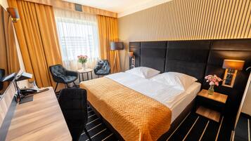 Een hotelkamer met een bed, een bureau, twee stoelen, een kleine tafel met een bloevas en een lamp.