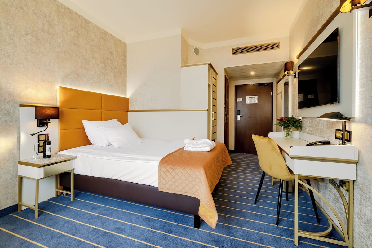 Een hotelkamer met een bed, nachtkastje, bureau, stoel en een spiegel.