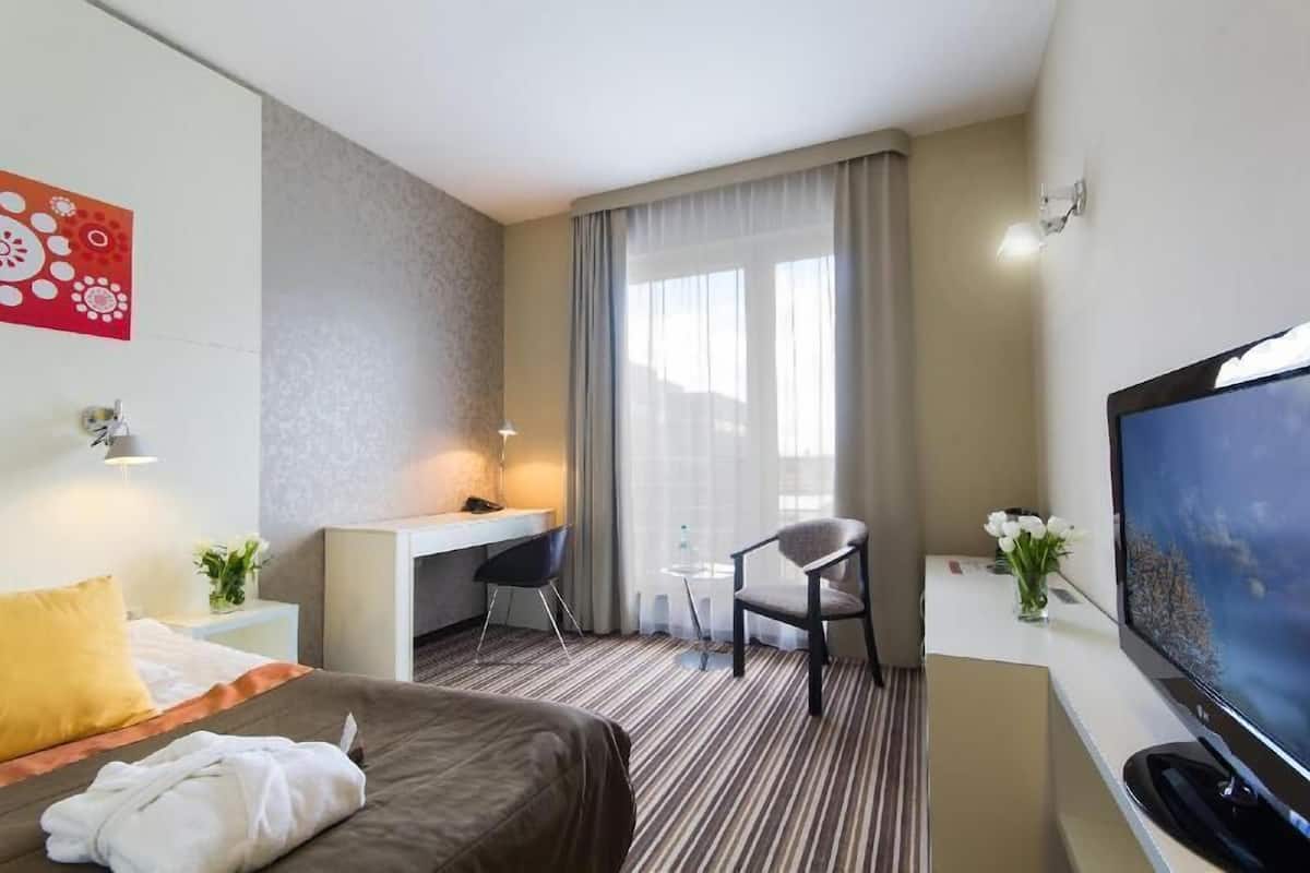 Een hotelkamer met een bed, bureau, stoel, televisie en raam met gordijnen.