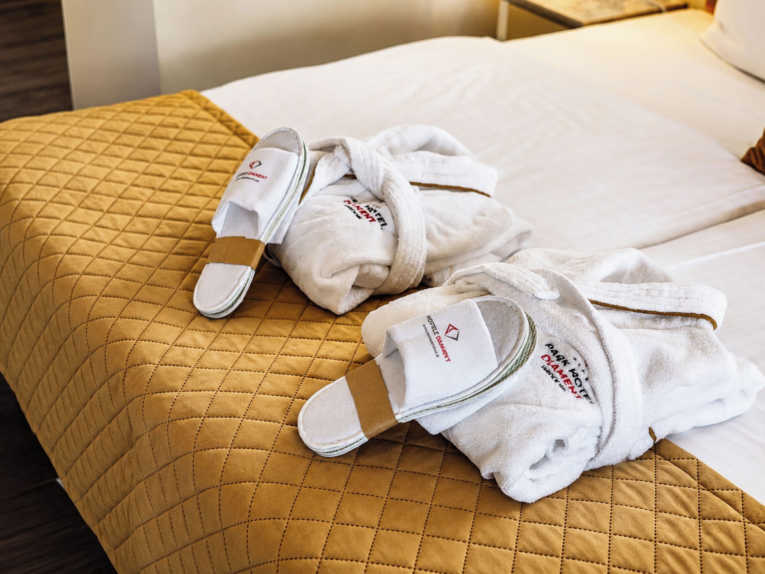 A bed with a quilted headboard and a folded white bathrobe and slippers on it.
