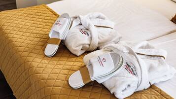 A bed with a quilted headboard and a folded white bathrobe and slippers on it.