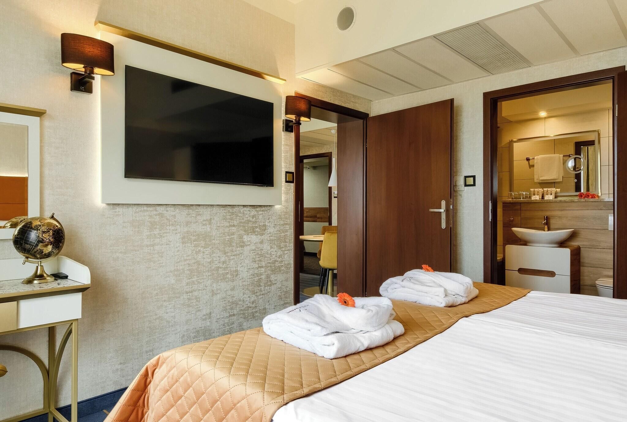 A hotel room with a bed, a television, a desk with a globe, and a bathroom visible through an open door.