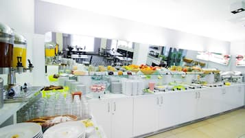 Una disposición tipo bufé con diversos alimentos y bebidas, vasos y platos apilados.
