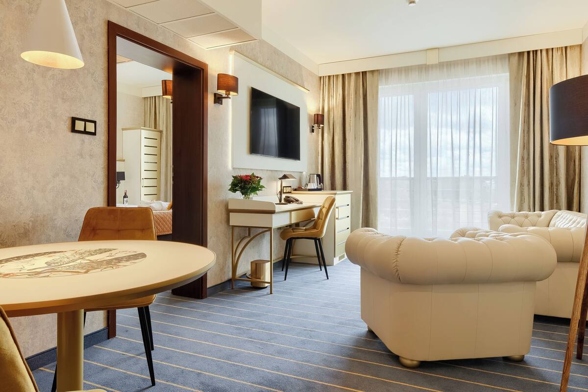 Een hotelkamer met een zithoek, een bank, een televisie en een groot raam met gordijnen.