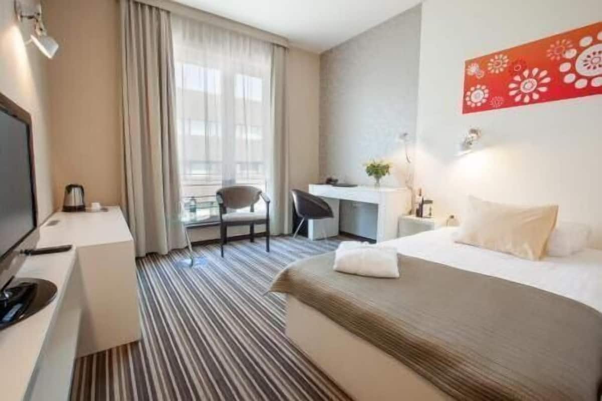 Hotelkamer met een bed, een bureau, een stoel, een televisie en een raam met gordijnen.