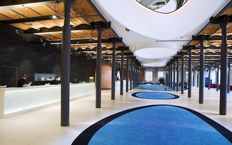 A spacious lobby with a modern design, featuring a reception desk, multiple seating areas, and a unique ceiling structure.