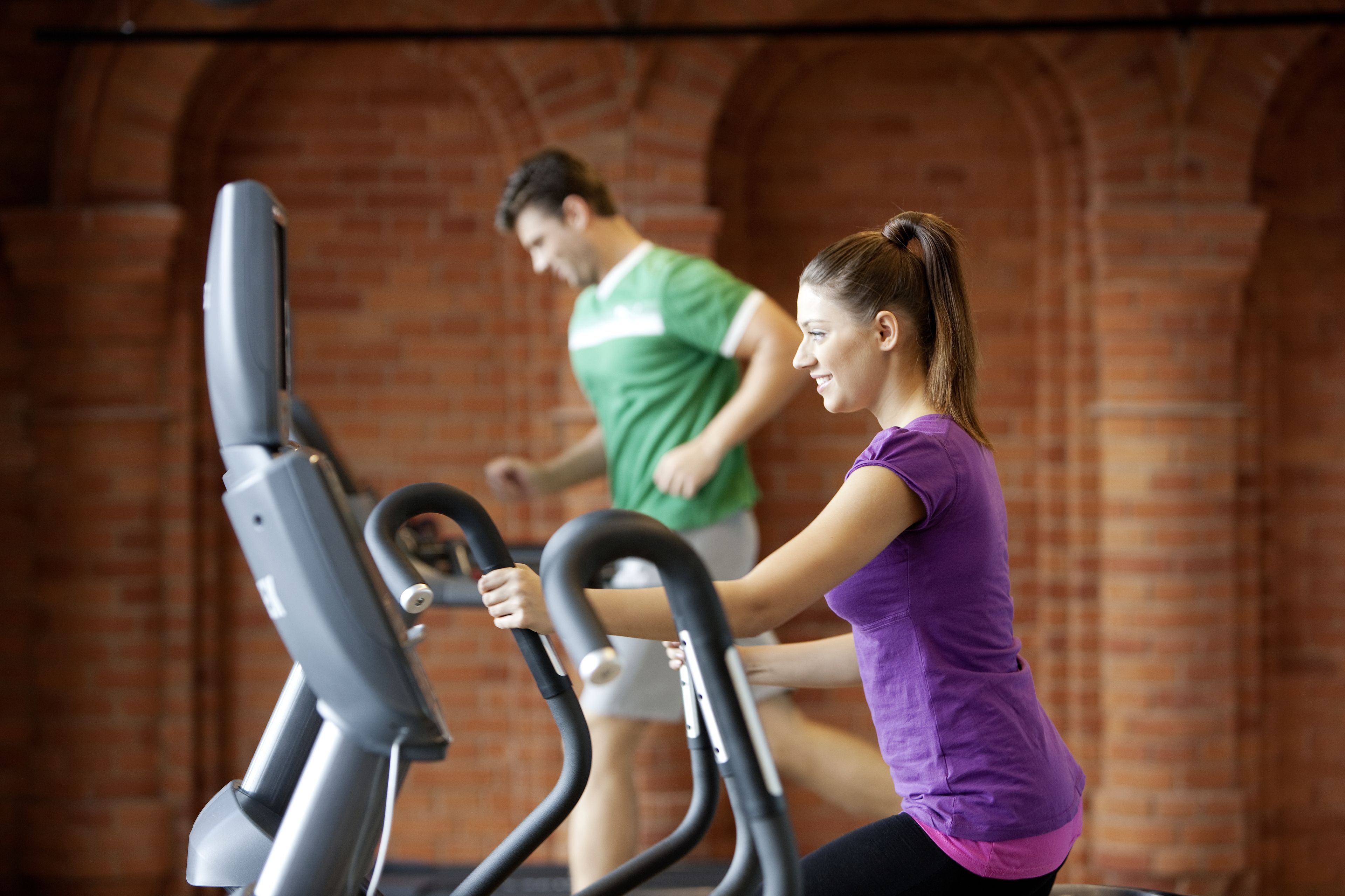 Two people using stationary bikes in a room with brick walls.