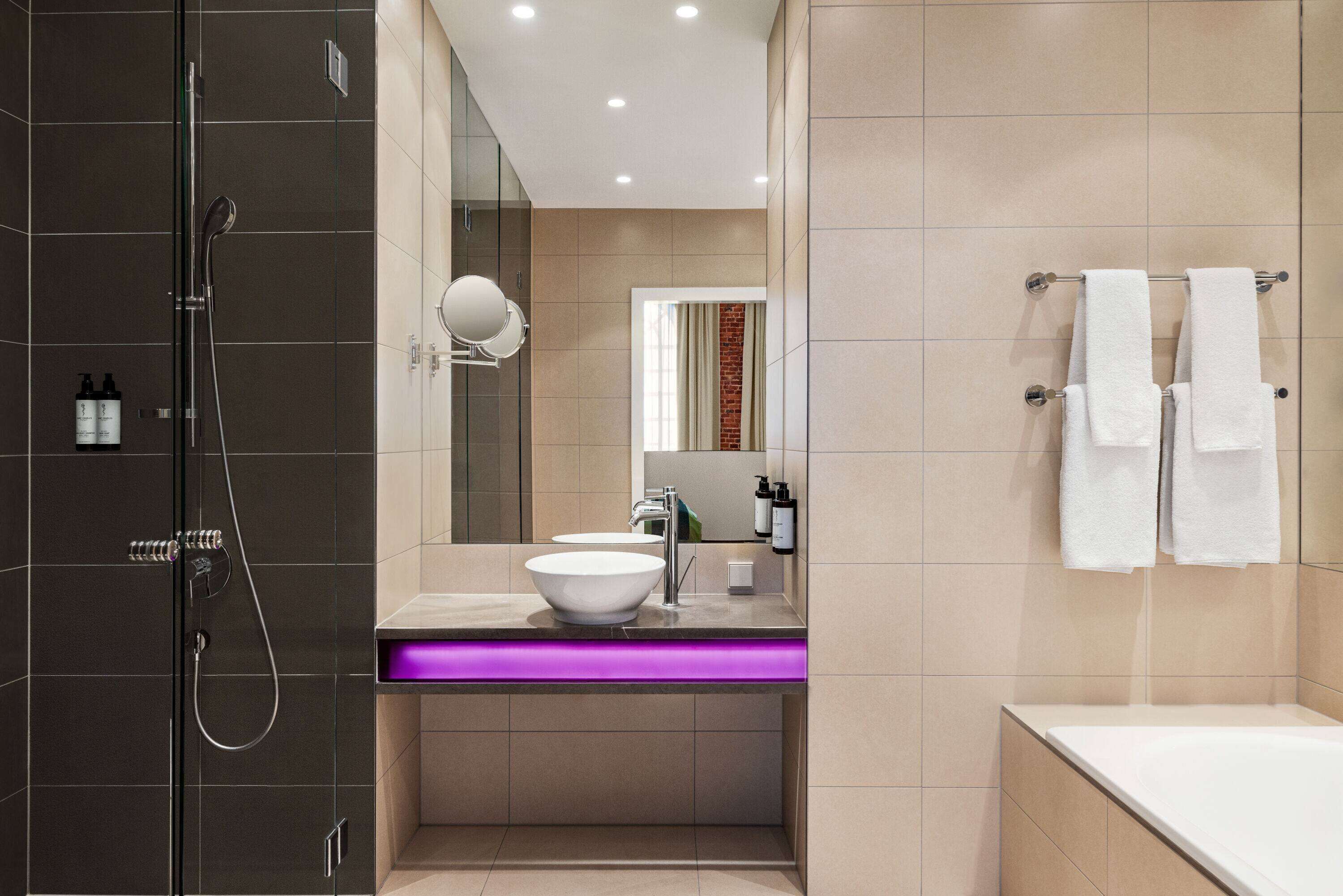 A modern bathroom with a glass-enclosed shower, a white sink with a purple-lit vanity, and a large mirror.