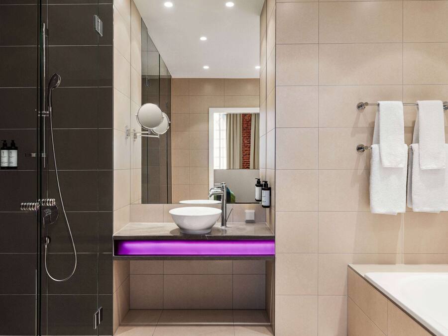 A modern bathroom with a glass-enclosed shower, a white sink with a purple-lit vanity, and a large mirror.