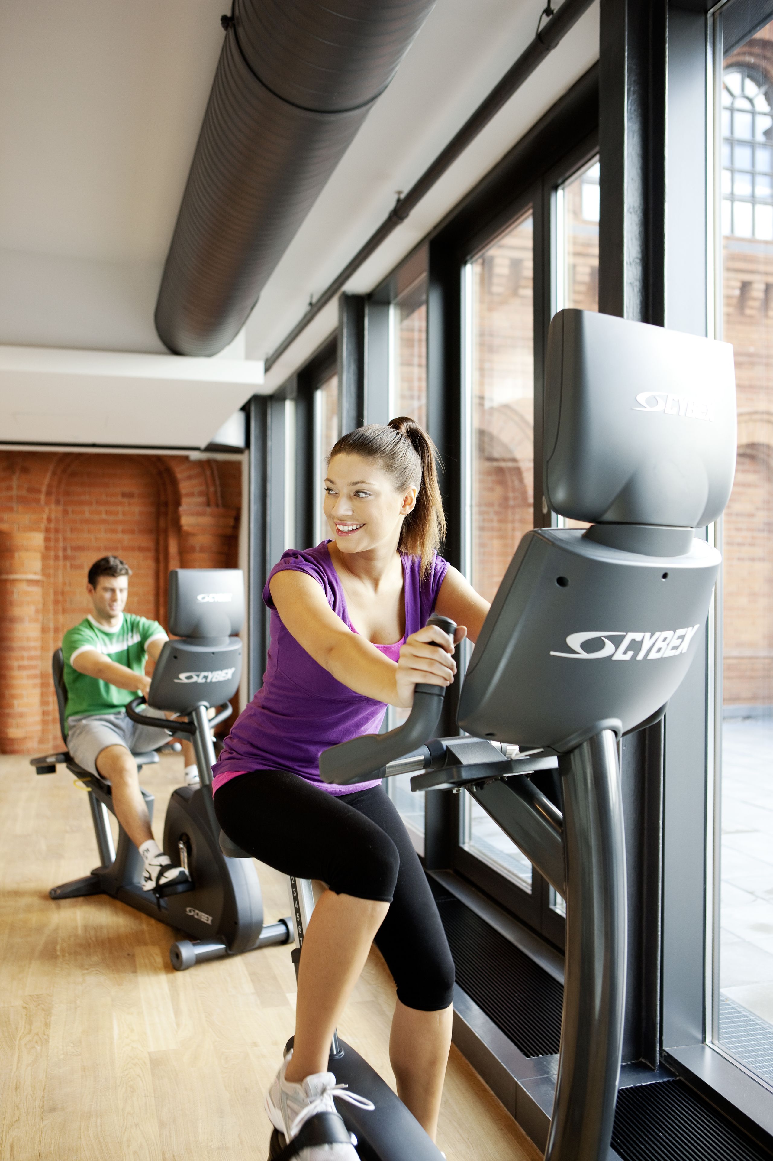 Une salle de sport équipée de vélos d’appartement, avec un mur en briques et de grandes fenêtres.