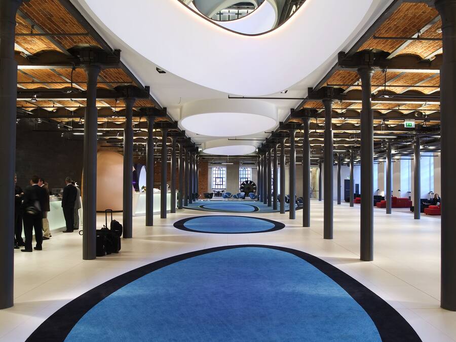 Un interior espacioso con una alfombra circular central, techos altos y un diseño arquitectónico moderno.