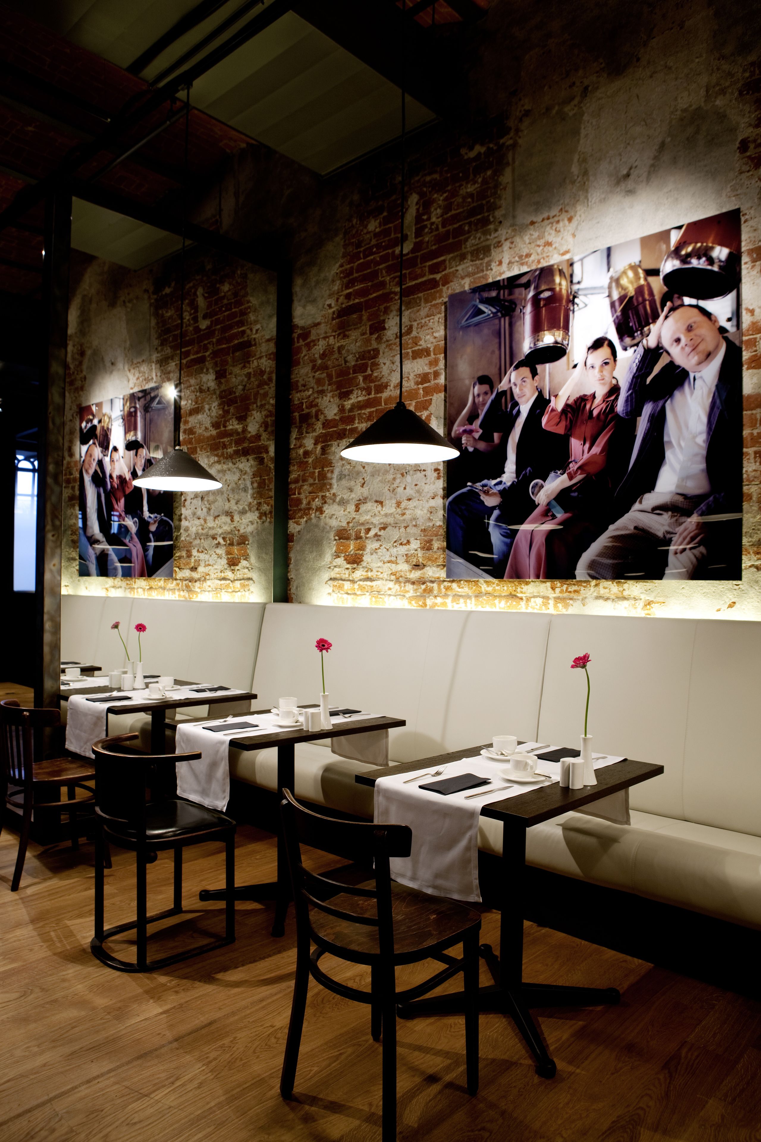 A restaurant interior with brick walls, wooden tables, and white cushioned seating.