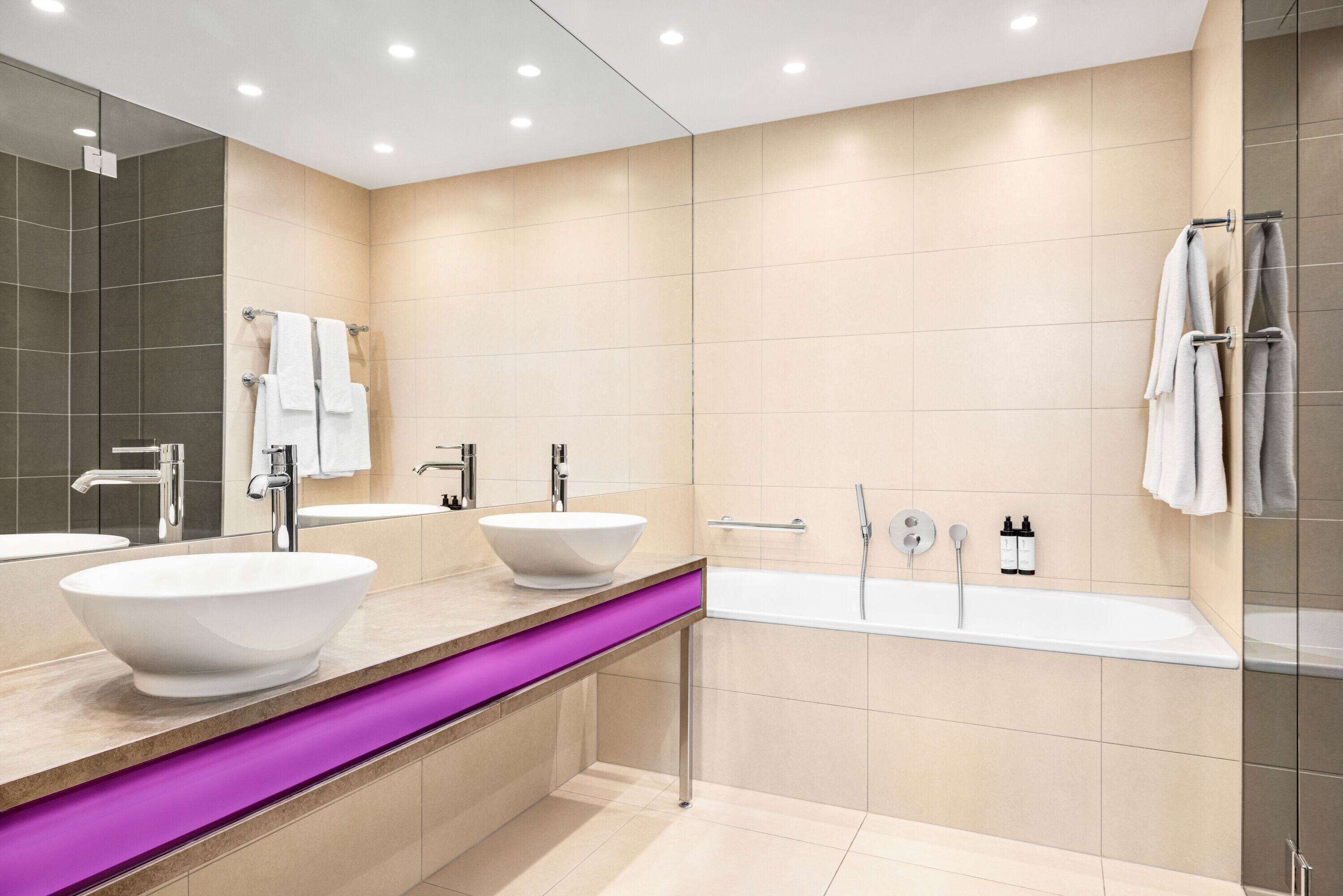 A modern bathroom with two sinks, a large bathtub, and a vanity with a purple accent.
