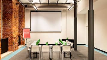 A conference room with a brick wall, a projector screen, and a table with chairs and green bottles.