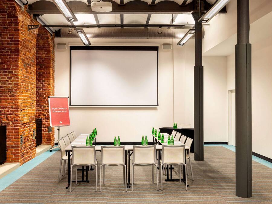 A conference room with a brick wall, a projector screen, and a table with chairs and green bottles.