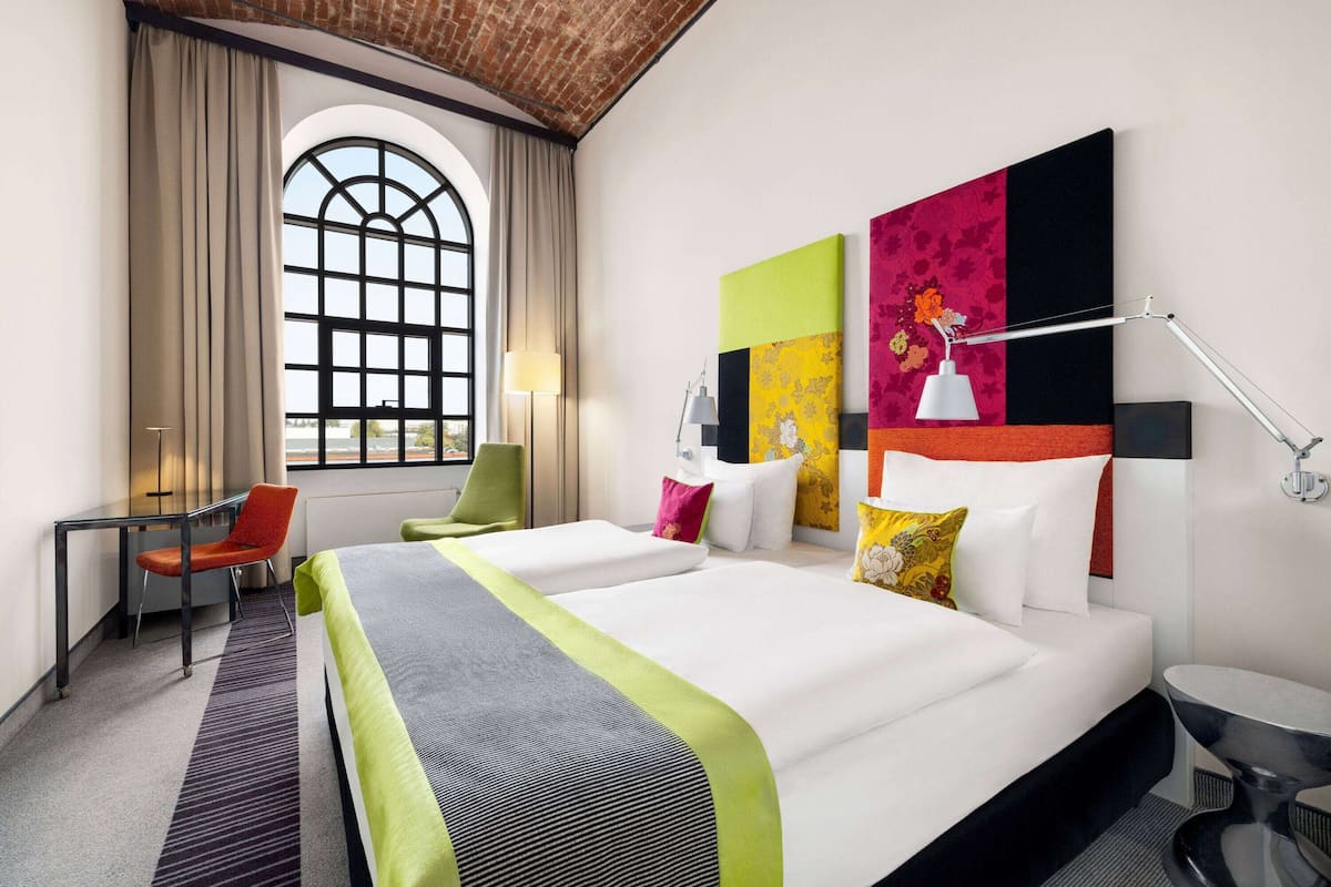 Una habitación de hotel con dos camas, un escritorio, una silla, un ventanal y un baño.