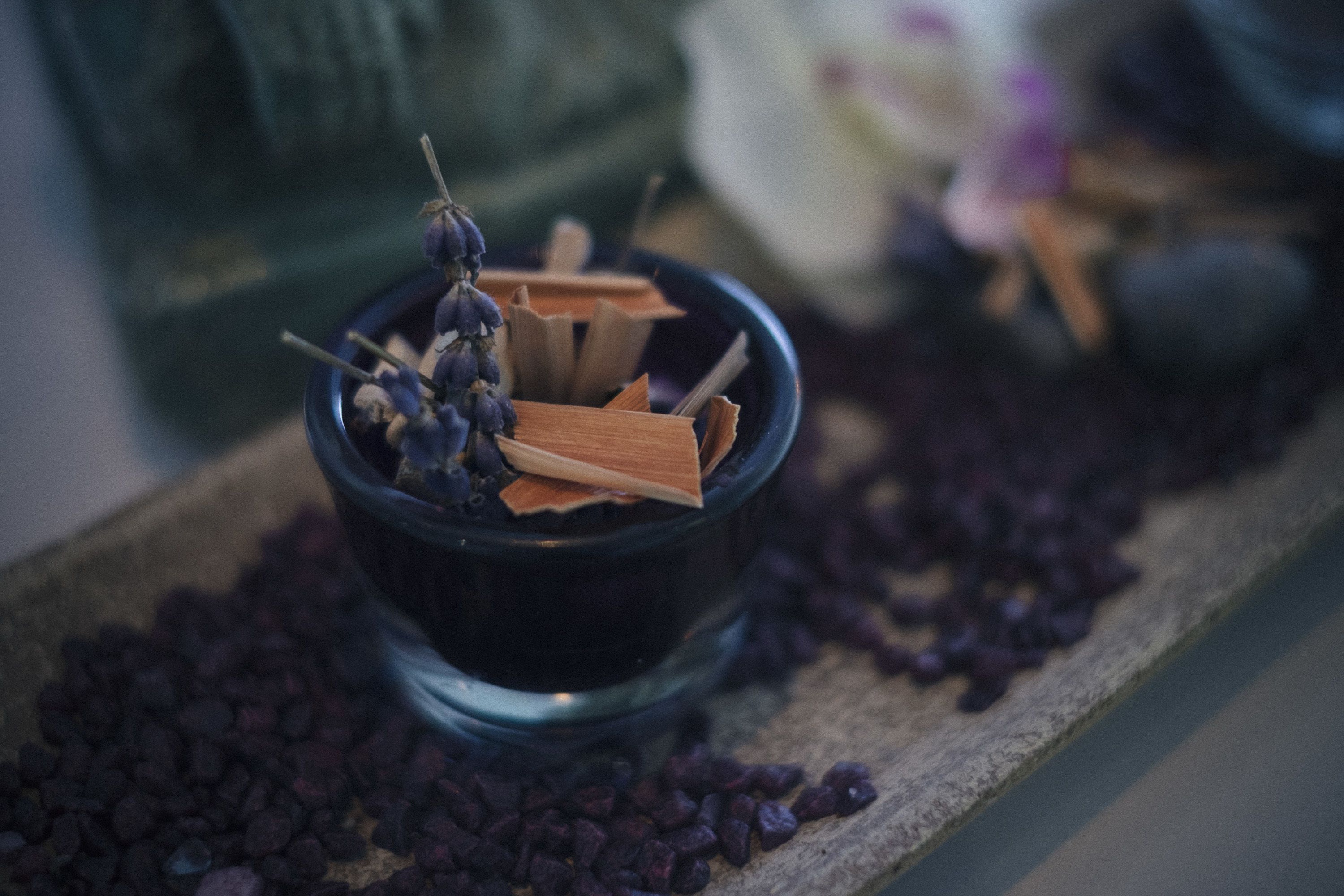 Eine kleine schwarze Schale mit getrockneten Kräutern und Stöckchen auf einer Holzschale.