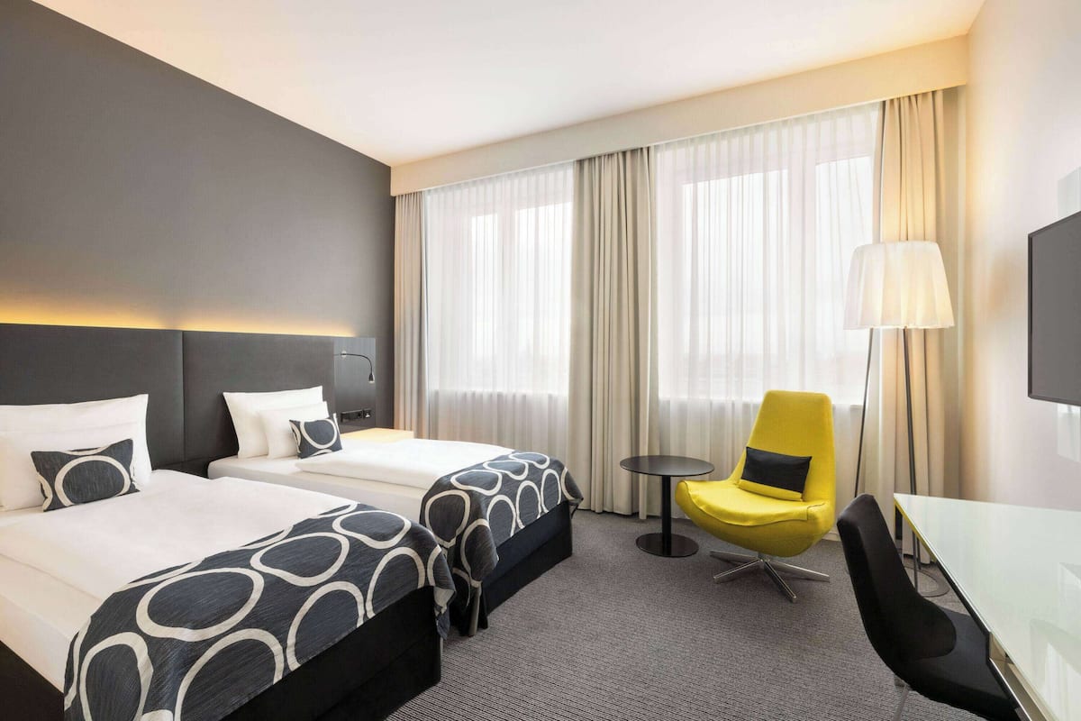 A hotel room with two beds, a yellow chair, a small table, and a TV.