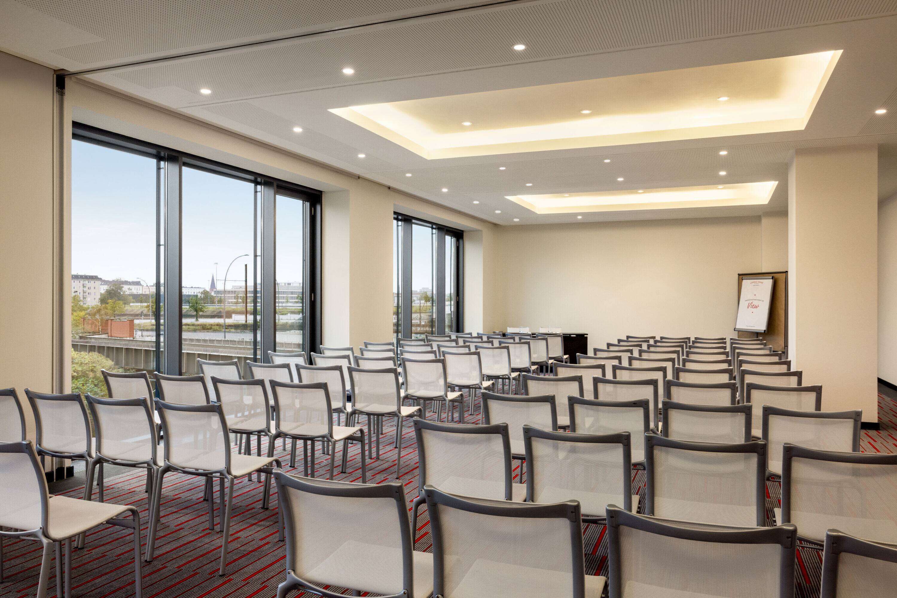 A conference room with rows of chairs, large windows, and a presentation screen.