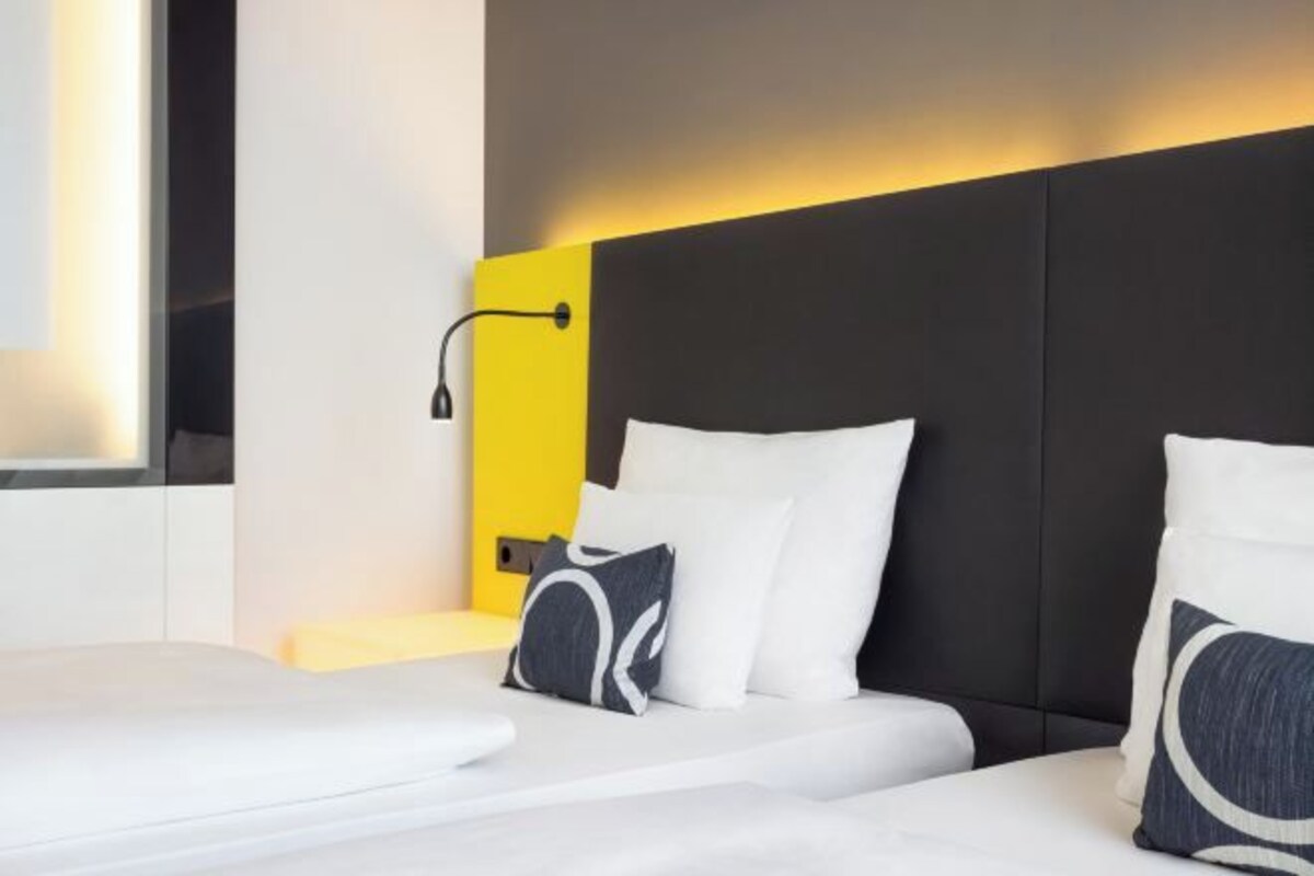 Una habitación de hotel moderna con cabecera negra, ropa de cama blanca y una pared de acento amarilla.