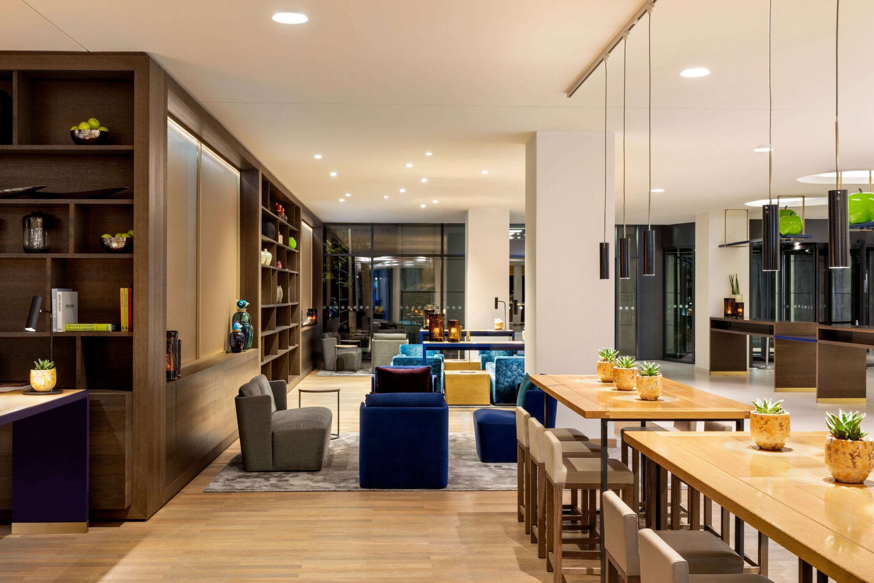 Ein modernes Interieur mit einem Holzesstisch, blauer Sitzgelegenheit und einer Bücherwand mit Büchern und Dekoration.