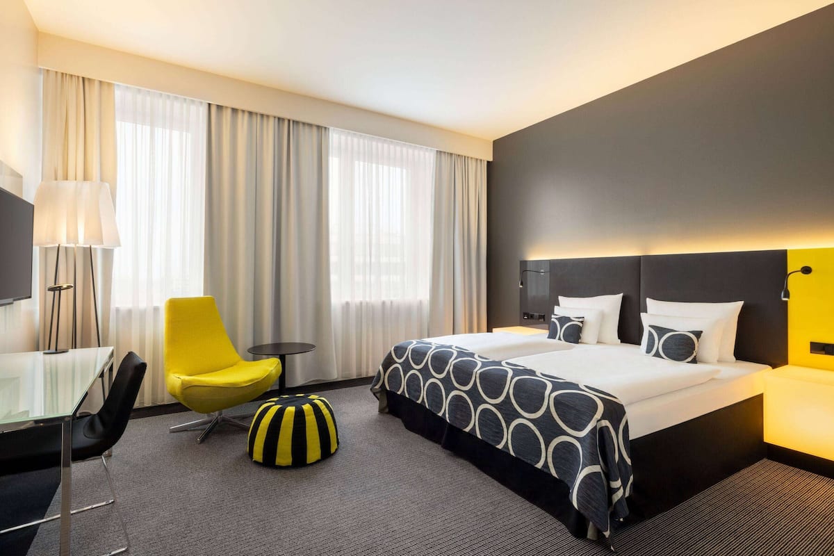 A hotel room with a bed, a desk, a chair, and a lamp.