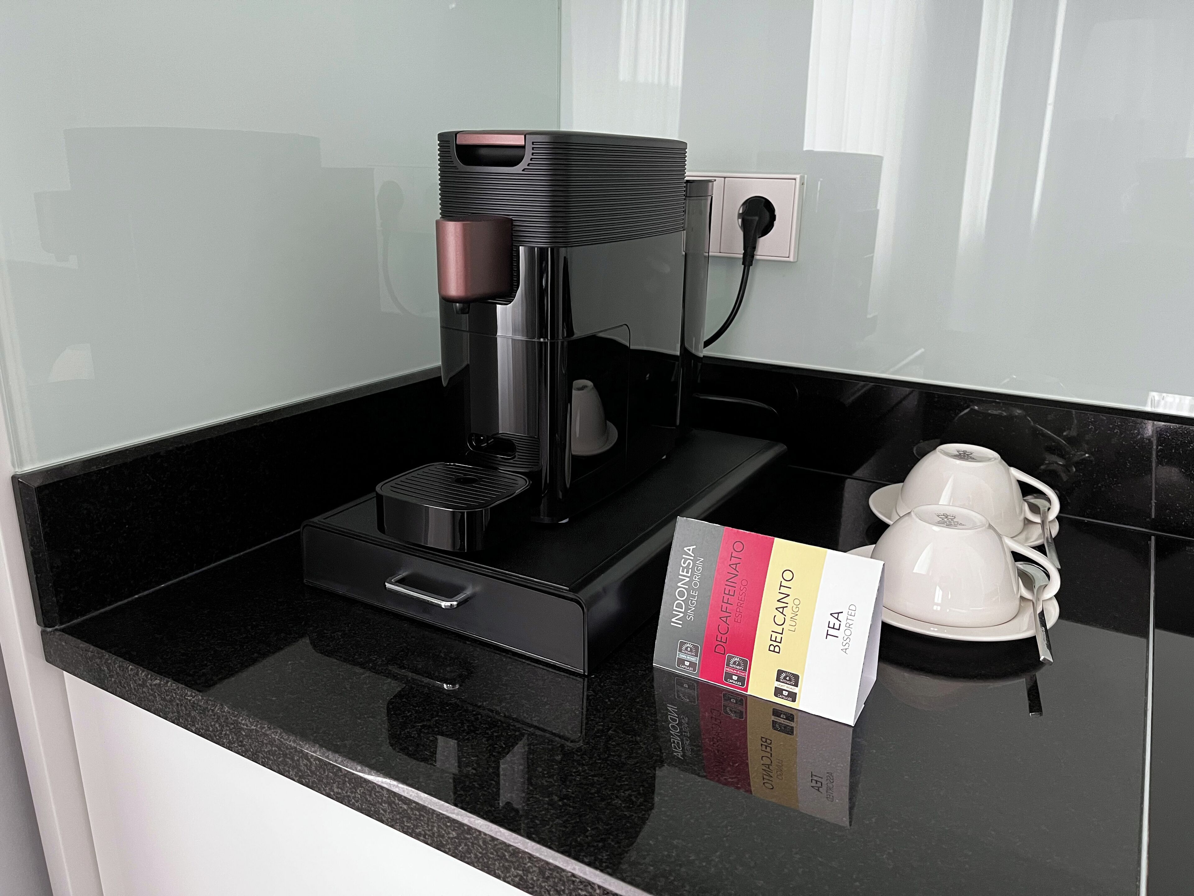 A coffee machine on a black countertop with a coffee pod holder and a box of assorted tea.