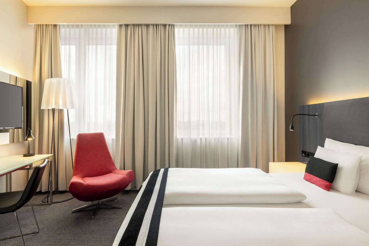 A hotel room with a bed, a desk with a chair, a TV, and a lamp.