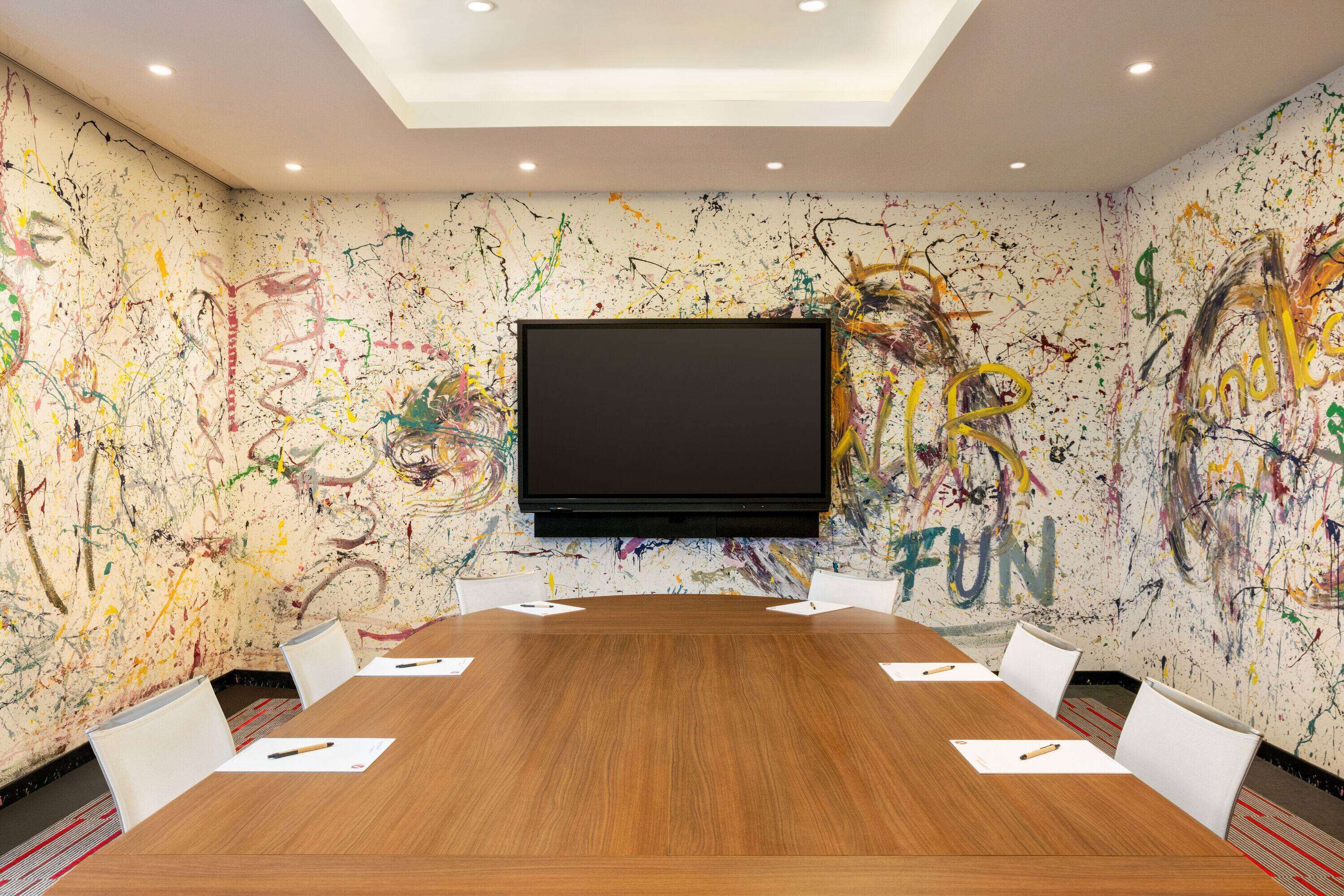 A conference room with a large table, white chairs, and a flat-screen TV mounted on the wall.