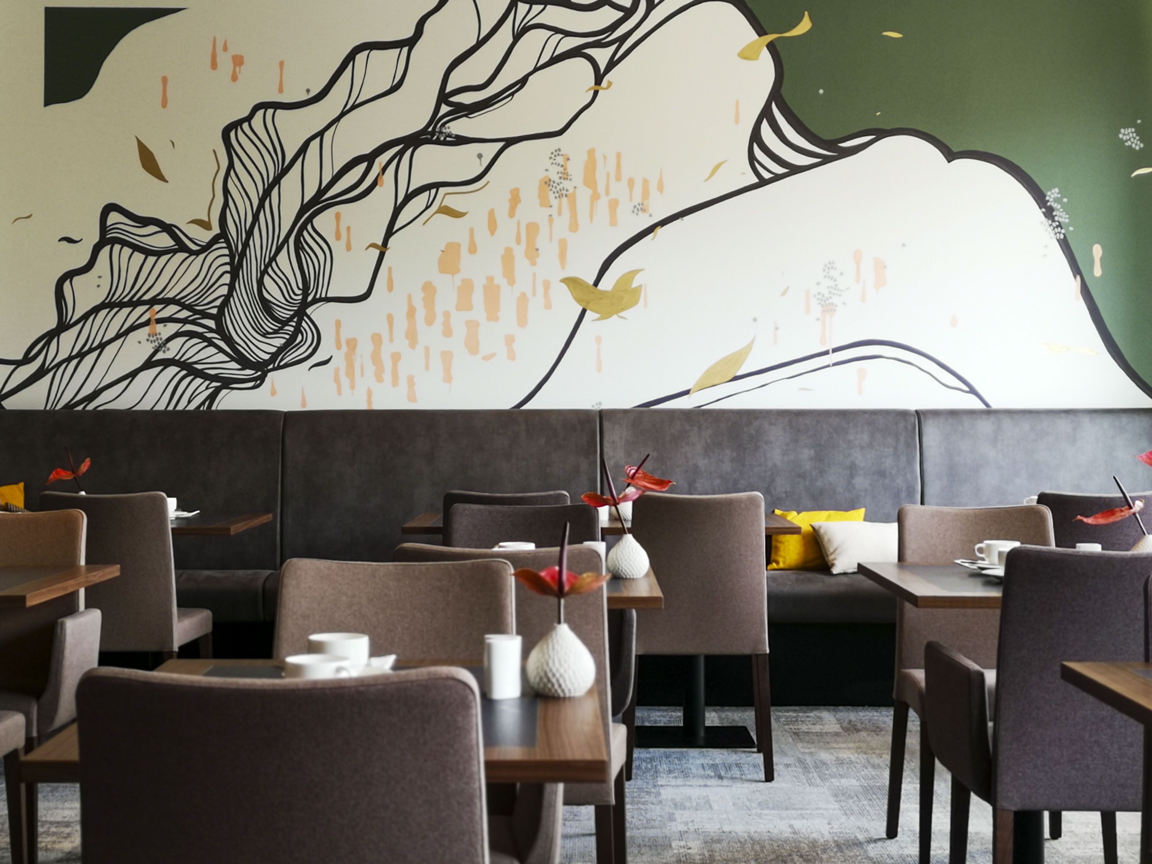 A restaurant with modern furniture, a mural on the wall, and a mix of seating arrangements.