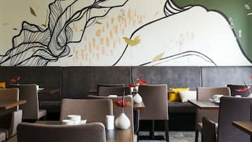 A restaurant with modern furniture, a mural on the wall, and a mix of seating arrangements.