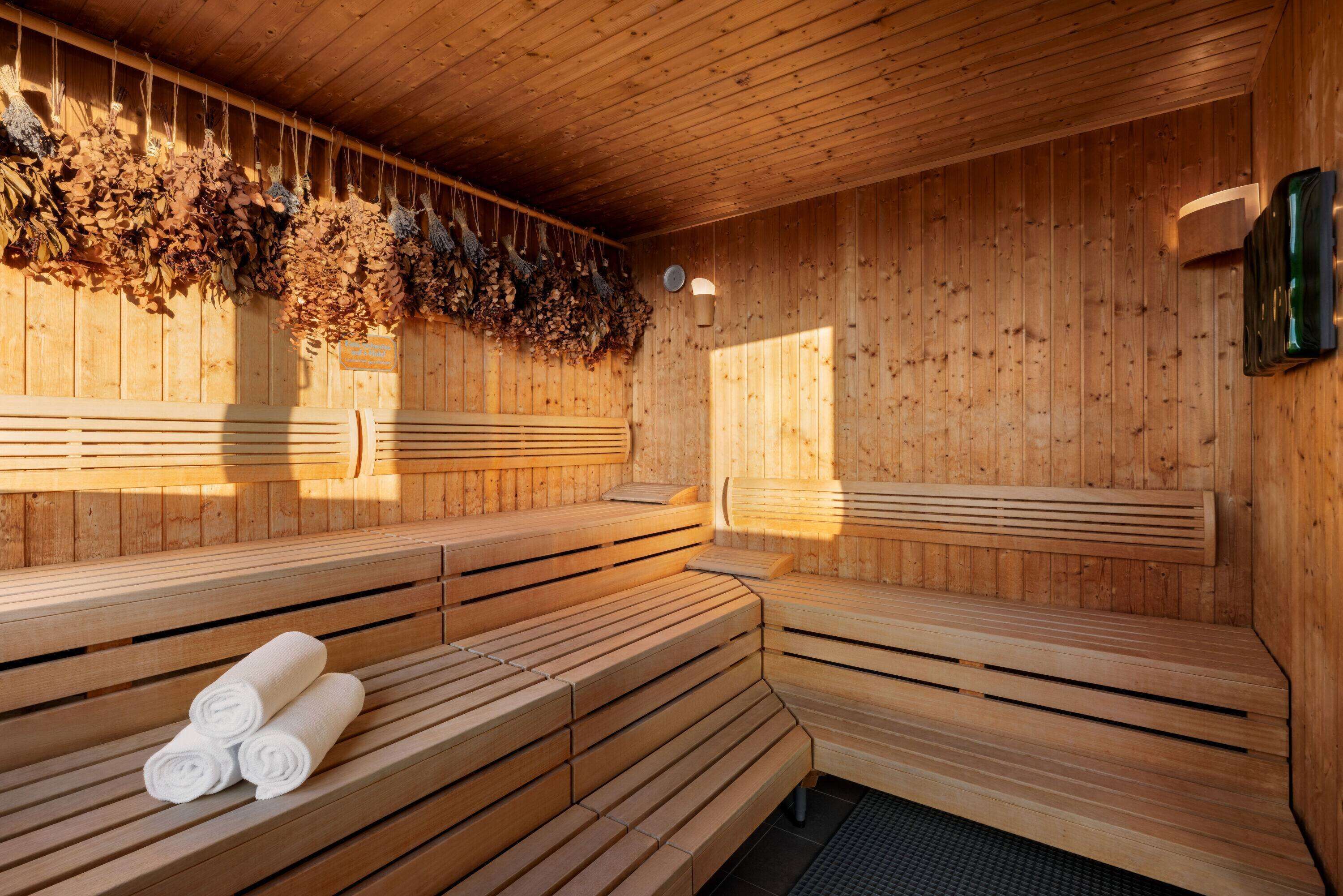 A wooden sauna with benches and hanging herbs.