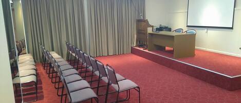 A conference room with rows of chairs, a podium, and a projection screen.