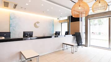 Un área de recepción moderna con un mostrador curvo, dos estaciones de trabajo con computadoras, un espacio de descanso y ventanas amplias.