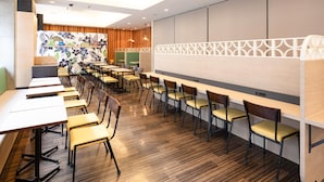 Une salle de conférence moderne, dotée de longues tables et de chaises, d’un grand tableau blanc et d’un mur décoratif orné d’un motif floral.