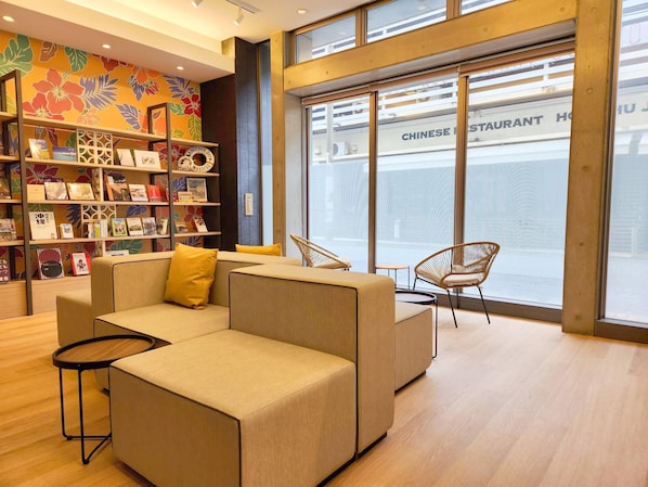 A modern interior with a sofa, chairs, a bookshelf, and a view of a Chinese restaurant through large windows.