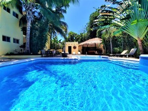 Una piscina rodeada de palmeras y sillas de descanso, con un edificio al fondo.