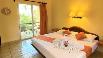 A hotel room with a bed, a ceiling fan, a sliding glass door to a balcony, and a wall-mounted lamp.