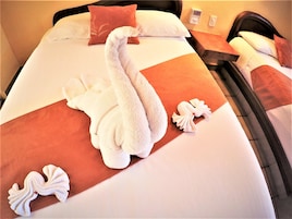 Habitación de hotel con una cama bien hecha y una toalla con forma de cisne, junto con dos toallas decorativas con forma de cisne sobre la cama.