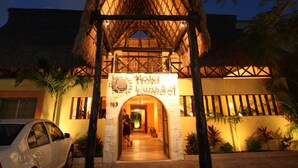 A hotel entrance with a thatched roof structure, a signboard, and a pathway leading inside.