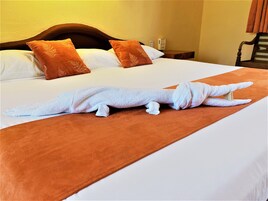 Un lit recouvert d’une couverture blanche et marron, avec deux oreillers marron et une serviette blanche disposée de manière à ressembler à un dinosaure.