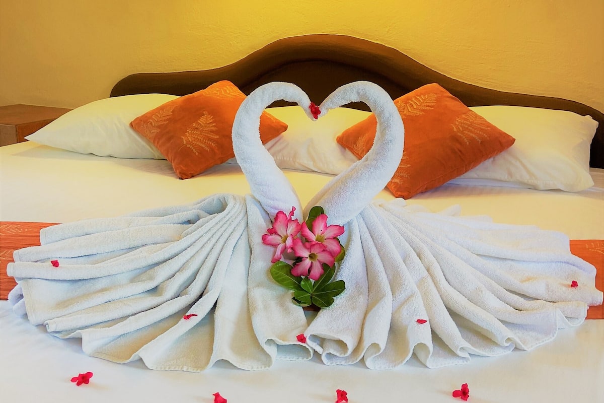 Un letto rifatto con un centrotavola a forma di cigno realizzato con asciugamani e cuscini arancioni.