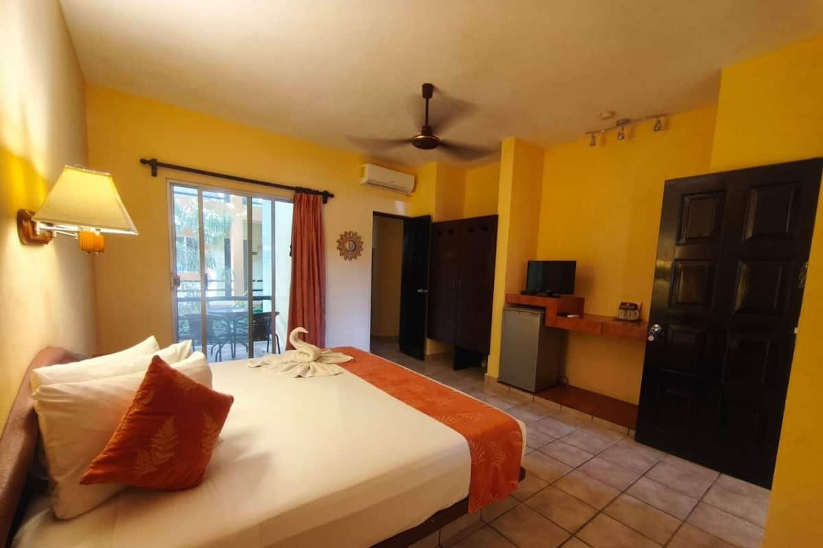 Una camera d'albergo con un letto, una ventola a soffitto, una televisione e una porta.
