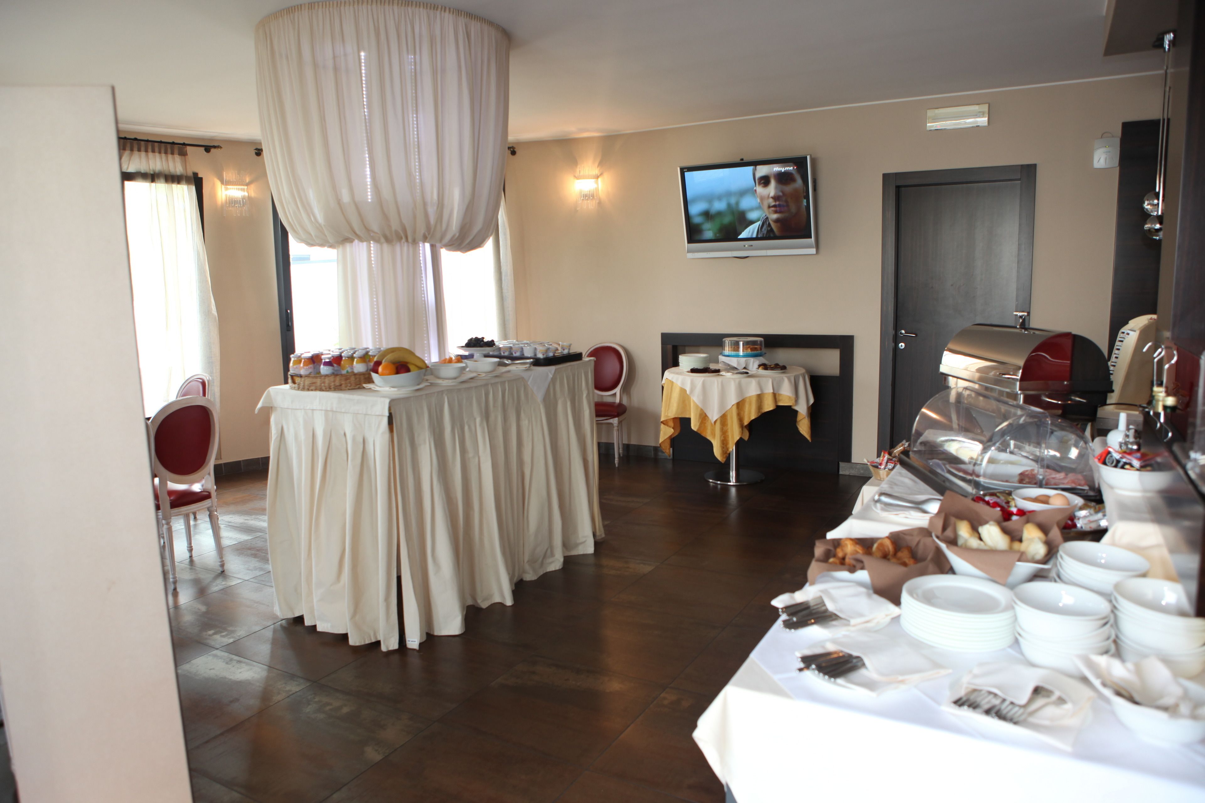Zona pranzo con tavoli apparecchiati per la colazione, una televisione a parete e un angolo barbecue.