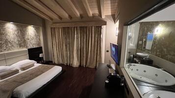 Una habitación de hotel con una cama grande, televisión, bañera y espejo.